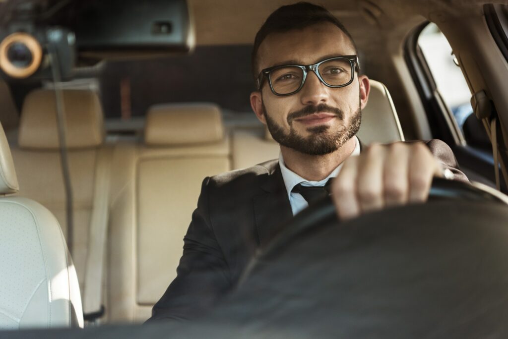 handsome cheerful driver in suit driving car